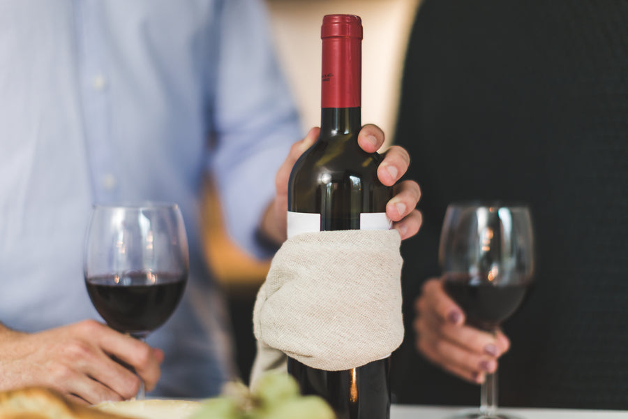 A bottle of red wine being presented beside two filled glasses
